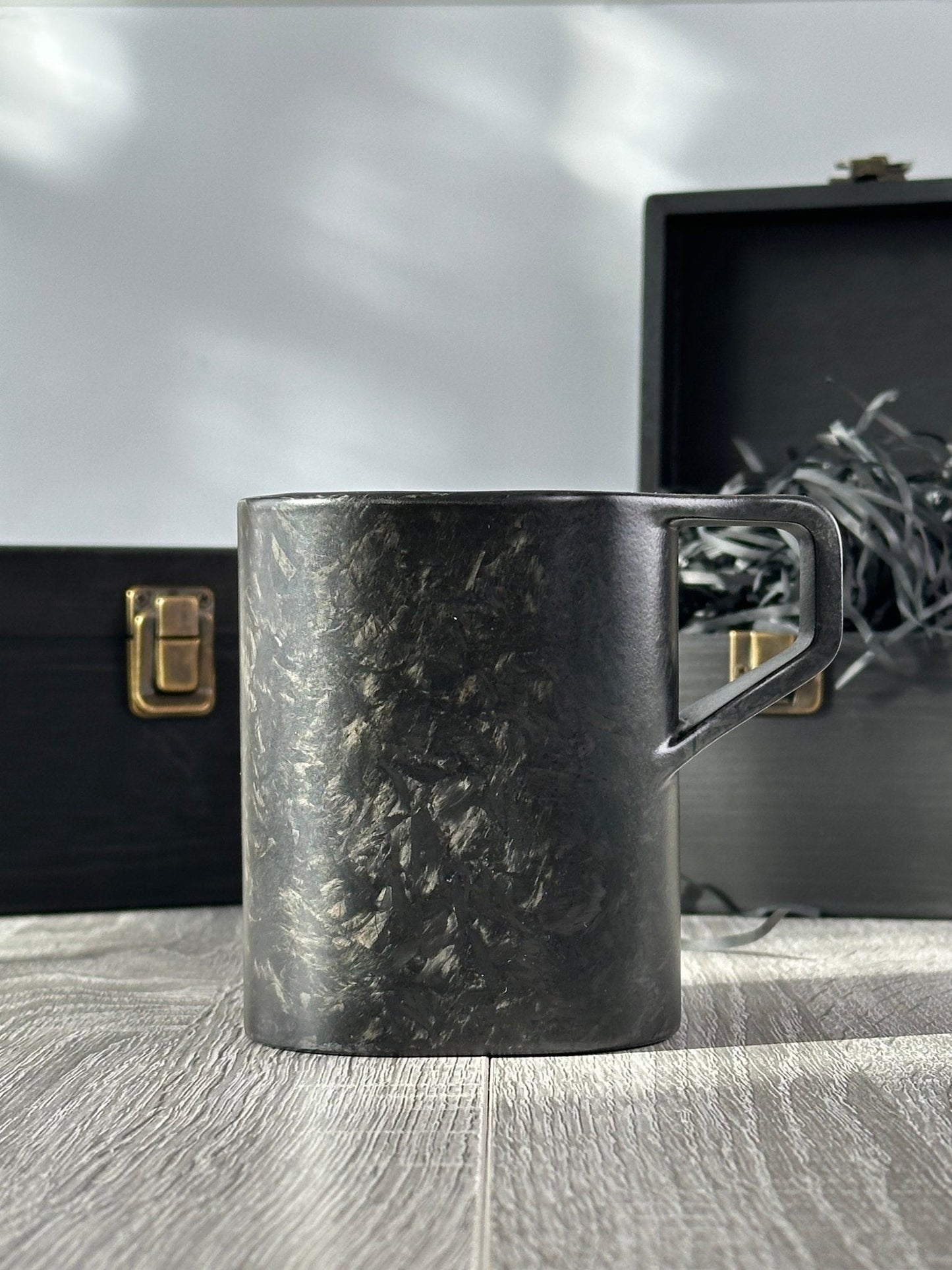Side profile of virgin carbon fibre mug – Quotidiano Edition 2 – with open and closed wooden boxes behind