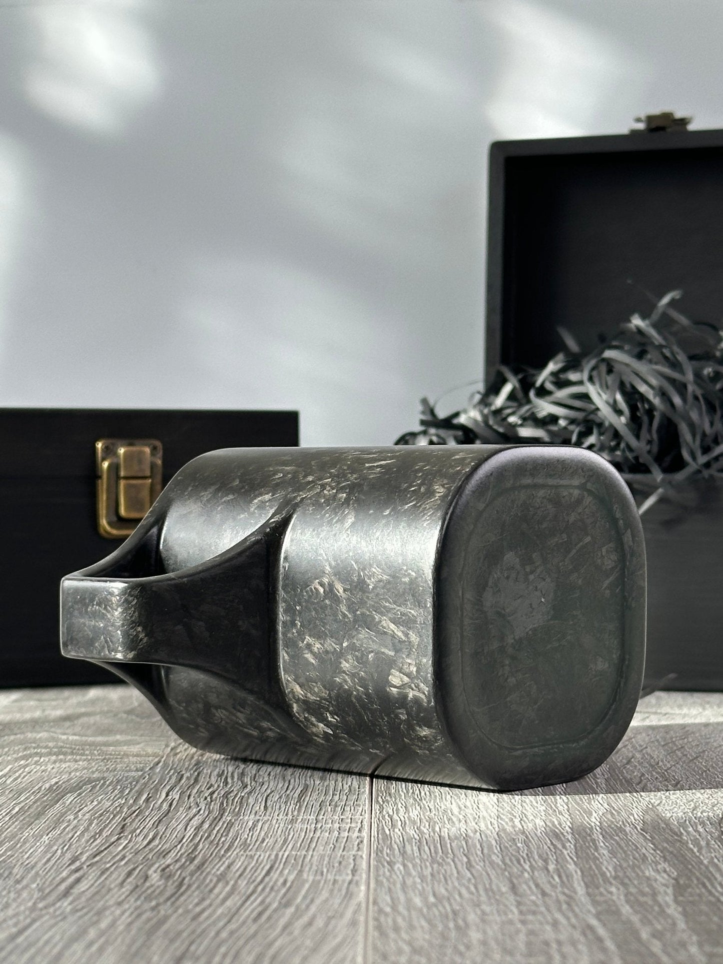 Bottom and under-handle view of carbon fiber mug, boxes in background