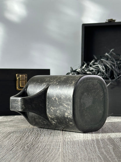 Bottom and under-handle view of carbon fiber mug, boxes in background