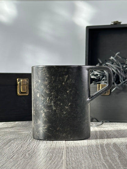 Side profile of virgin carbon fiber mug with open and closed wooden boxes behind